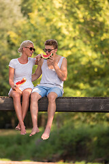 Image showing couple enjoying watermelon while sitting on the wooden bridge