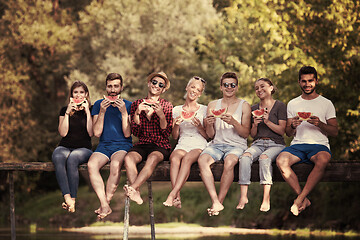 Image showing friends enjoying watermelon while sitting on the wooden bridge