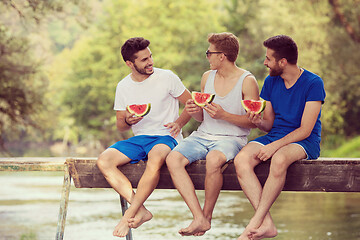 Image showing men enjoying watermelon while sitting on the wooden bridge