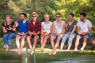 Image showing friends enjoying watermelon while sitting on the wooden bridge