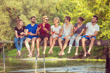 Image showing friends enjoying watermelon while sitting on the wooden bridge