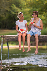 Image showing couple enjoying watermelon while sitting on the wooden bridge