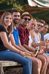 Image showing friends enjoying watermelon while sitting on the wooden bridge