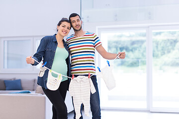 Image showing young couple holding baby bodysuits at home