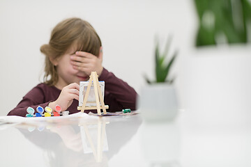 Image showing little girl painting on canvas and hiding face