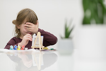 Image showing little girl painting on canvas and hiding face