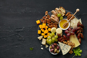 Image showing Top view of tasty cheese plate with fruit on the black stone