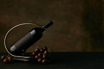 Image showing Front view of tasty grapes plate with the wine bottle on dark studio background