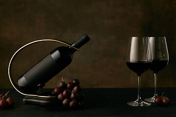 Image showing Front view of tasty grapes plate with the wine bottle on dark studio background