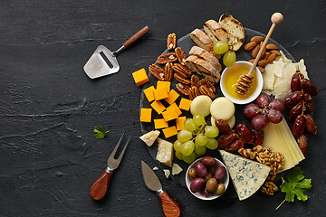 Image showing Top view of tasty cheese plate with fruit on the black stone