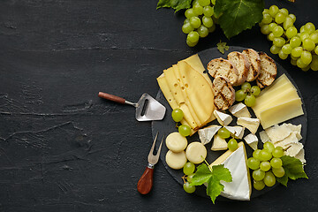 Image showing Top view of tasty cheese plate with fruit on the black stone