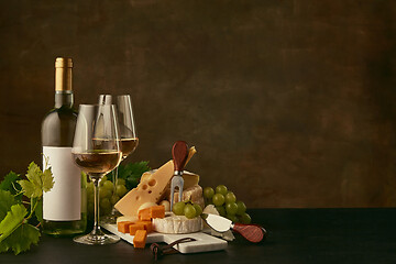 Image showing Front view of tasty cheese plate with the wine bottle on dark studio background