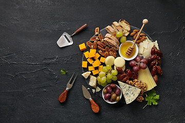 Image showing Top view of tasty cheese plate with fruit on the black stone