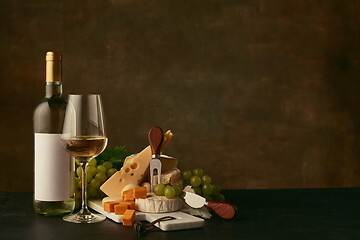 Image showing Front view of tasty cheese plate with the wine bottle on dark studio background