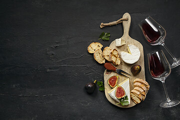 Image showing Two glasses of red wine and cheese plate with fruit on the black stone