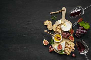 Image showing Two glasses of red wine and cheese plate with fruit on the black stone
