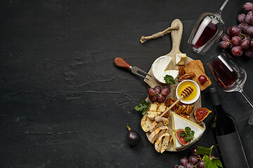 Image showing Two glasses of red wine and cheese plate with fruit on the black stone