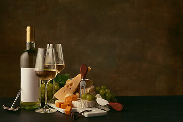 Image showing Front view of tasty cheese plate with the wine bottle on dark studio background