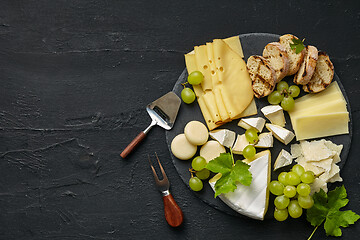 Image showing Top view of tasty cheese plate with fruit on the black stone