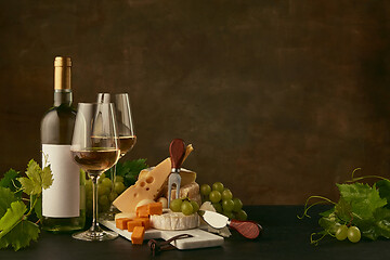 Image showing Front view of tasty cheese plate with the wine bottle on dark studio background