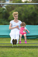 Image showing mother and little daughter swinging at backyard