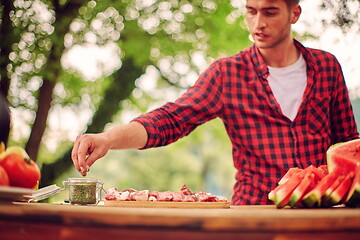 Image showing man putting spices on raw meat for barbecue
