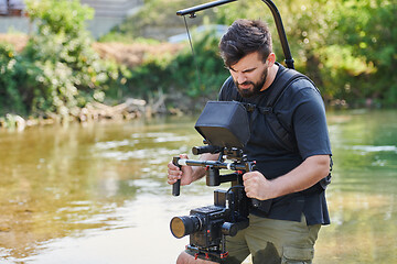 Image showing a professionally equipped cameraman shoots in the water surrounded by beautiful nature.