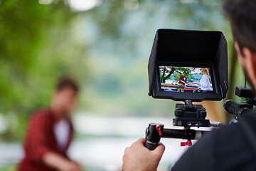 Image showing a professionally equipped cameraman is filming a group of people having dinner by the river.