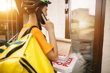 Image showing Young man as a courier delivering pizza using gadgets