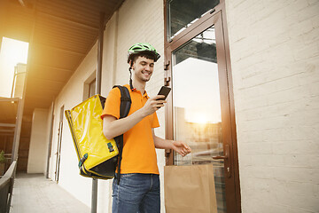 Image showing Young man as a courier delivering pizza using gadgets