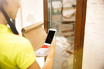 Image showing Young woman as a courier delivering pizza using gadgets