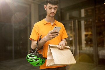 Image showing Young man as a courier delivering package using gadgets