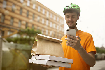 Image showing Young man as a courier delivering pizza using gadgets