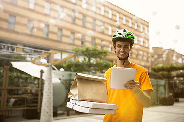 Image showing Young man as a courier delivering pizza using gadgets