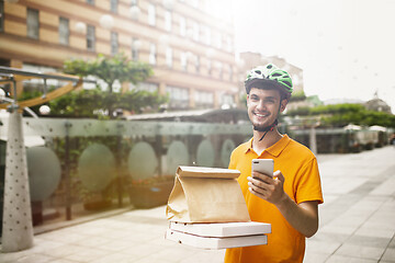 Image showing Young man as a courier delivering pizza using gadgets