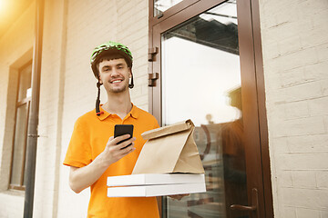 Image showing Young man as a courier delivering pizza using gadgets