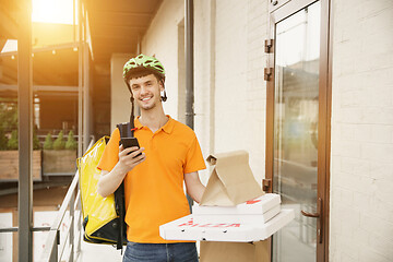 Image showing Young man as a courier delivering pizza using gadgets