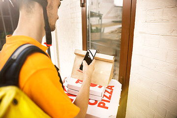 Image showing Young man as a courier delivering pizza using gadgets