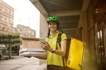 Image showing Young woman as a courier delivering pizza using gadgets