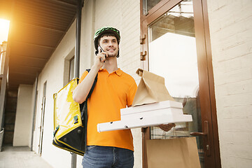 Image showing Young man as a courier delivering pizza using gadgets