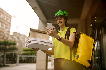 Image showing Young woman as a courier delivering pizza using gadgets