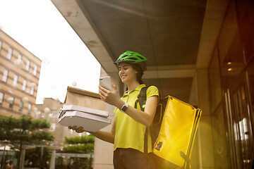 Image showing Young woman as a courier delivering pizza using gadgets