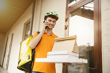 Image showing Young man as a courier delivering pizza using gadgets