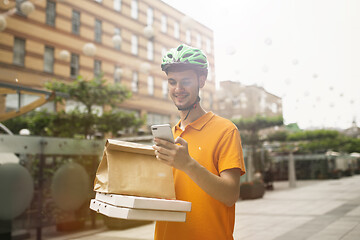 Image showing Young man as a courier delivering pizza using gadgets