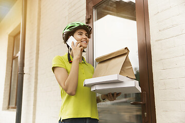 Image showing Young woman as a courier delivering pizza using gadgets