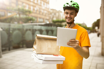 Image showing Young man as a courier delivering pizza using gadgets