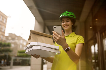 Image showing Young woman as a courier delivering pizza using gadgets