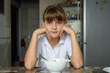 Image showing The girl is sitting at the table in the kitchen, in front of her is an empty plate, the girl looks into the frame