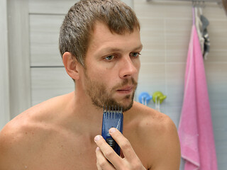 Image showing A man in a bathroom cuts a heavily regrown beard