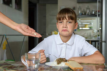 Image showing The girl does not like the medicines offered by her mother before dinner